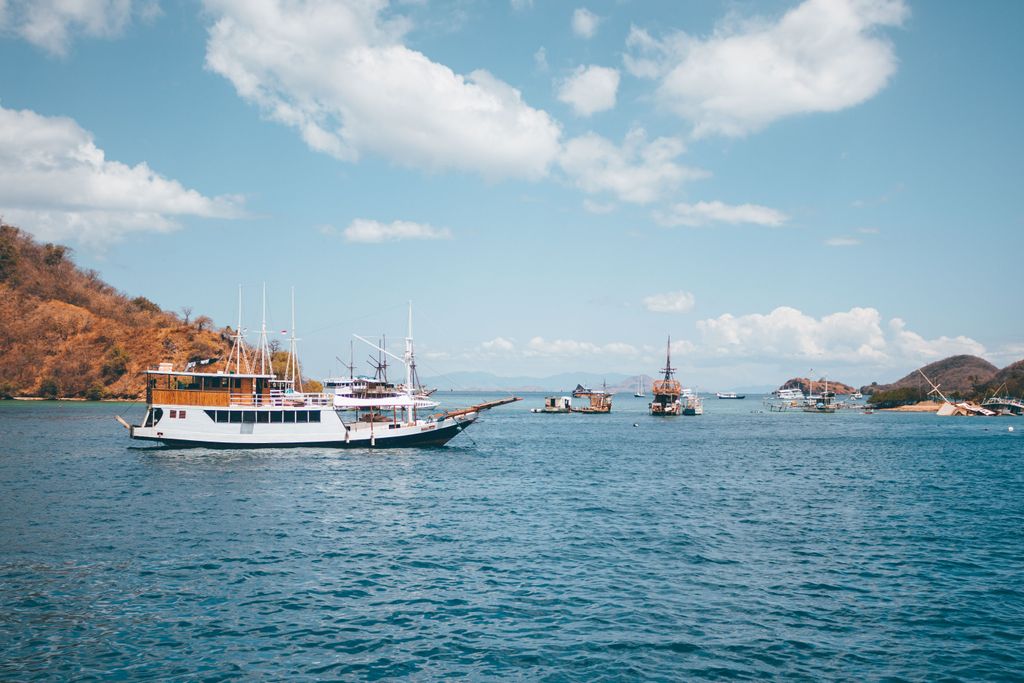 Traditional ships sailing in the clear waters of Komodo & Flores Indonesia under a sunny sky.
